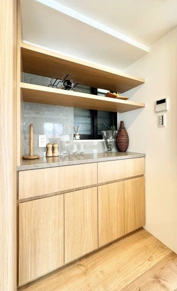 木製のキャビネット上の棚にガラス器と飾り物、壁にはスイッチと温度計