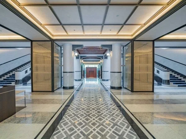 豪華なビルのエントランスホール。中央に通路があり、その両側に階段と金色の装飾壁が配置されている。天井は格子模様。