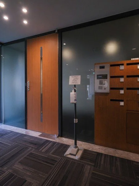 木製のドアとガラス扉のある室内、入口付近に消毒液の自動噴霧器と掲示板があります。