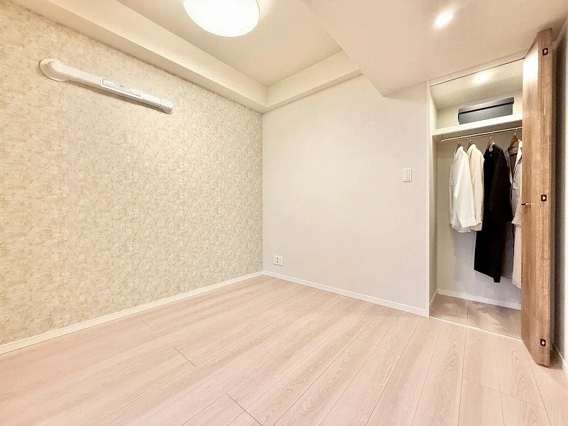 白とベージュの壁と床の空間に、クローゼットに衣服が掛かっているシンプルな室内