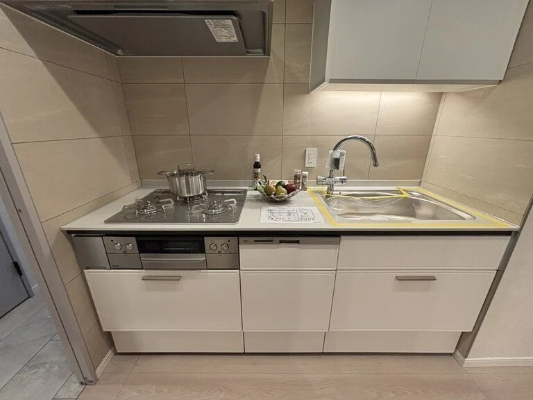 キッチンのカウンターに調理器具と調味料、果物のバスケットが置かれている。シンクとガスコンロが備わっている。