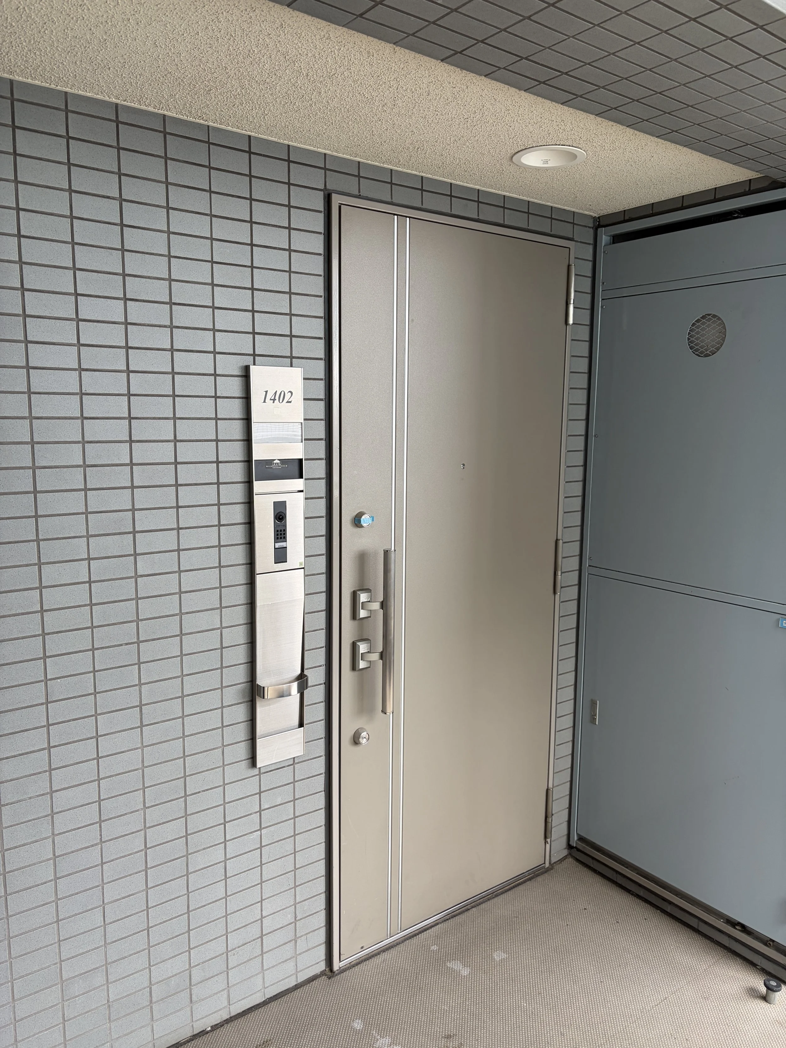 ビルの入り口の扉とインターホン、番号1402のプレートが付いた壁。