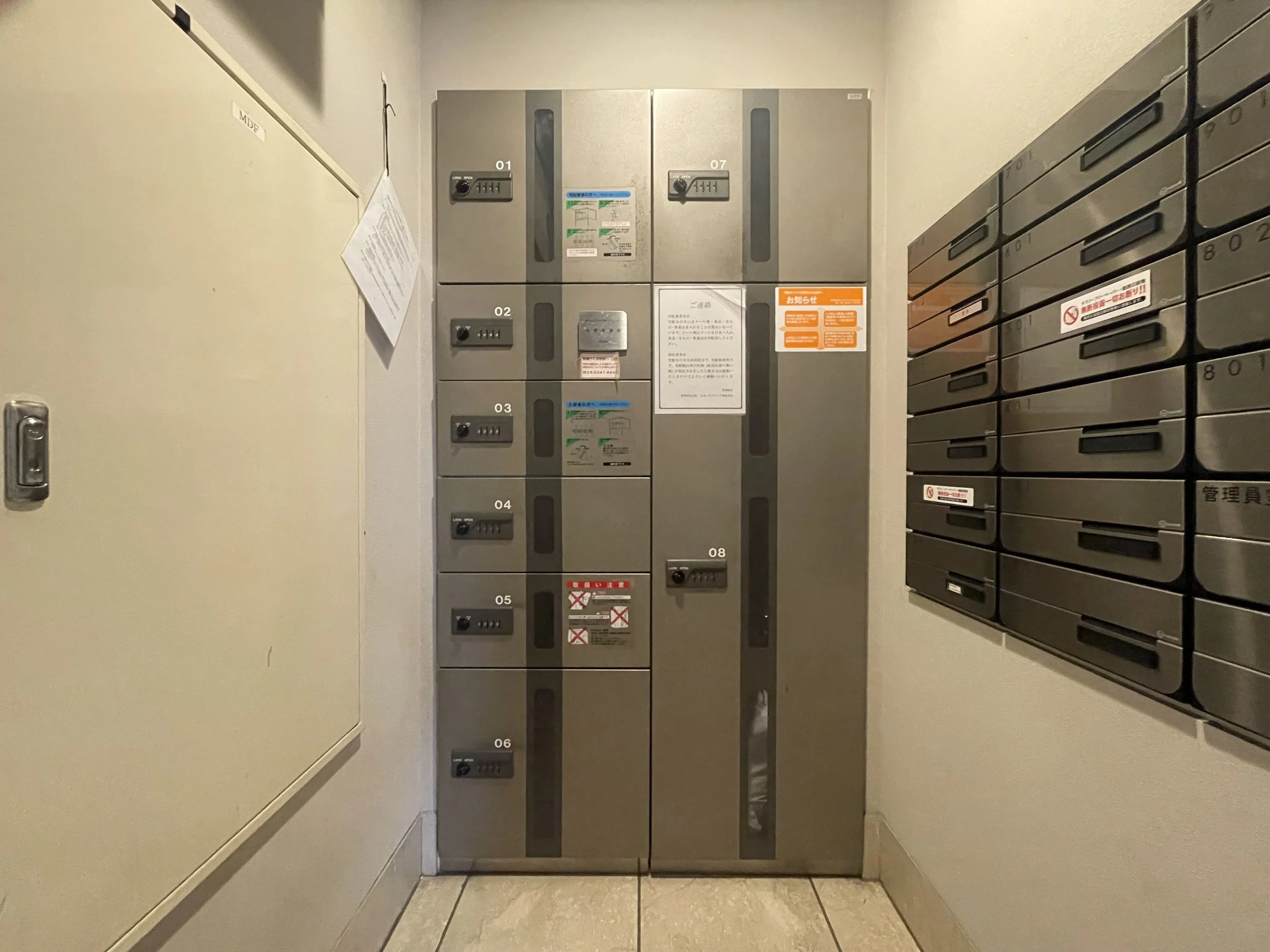 コインロッカーと郵便ポストの写真。コインロッカーには番号が書かれ、いくつかにロックがかかっている。壁にはいくつかの貼り紙があります。