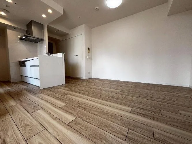 空のリビングルームとキッチンエリア、木製の床と白い壁、シンプルな内装