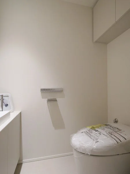 白い壁と収納キャビネット、トイレの便座カバーに包装されたトイレ便器