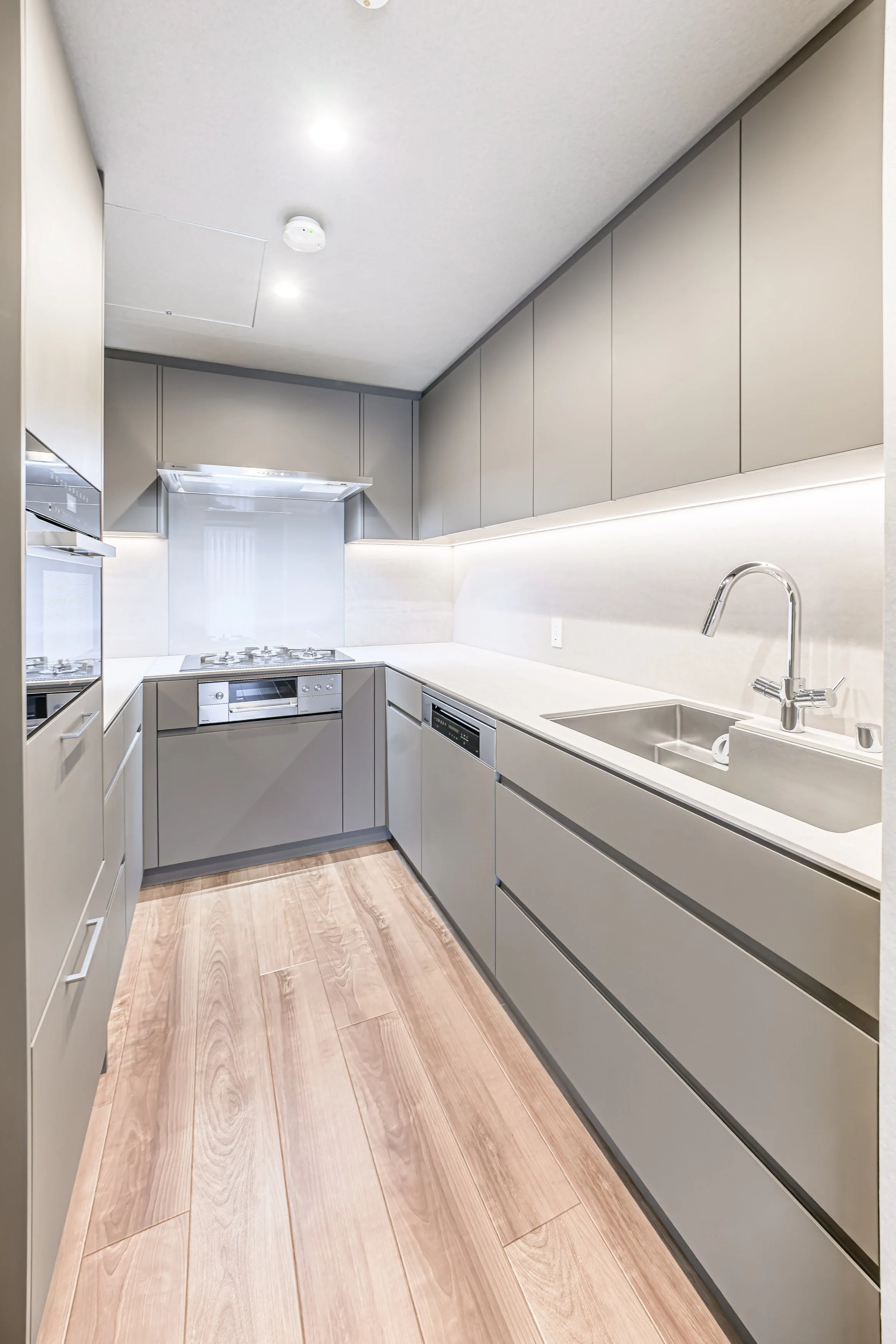 シンプルでモダンなキッチン、淡いグレーのキャビネット、白いカウンターと壁、ダーク木目調の床