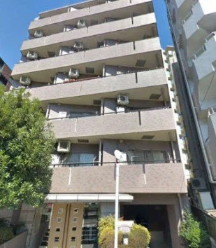 中層のコンクリート製のマンションの外観とバルコニー、空調機器と窓が見える