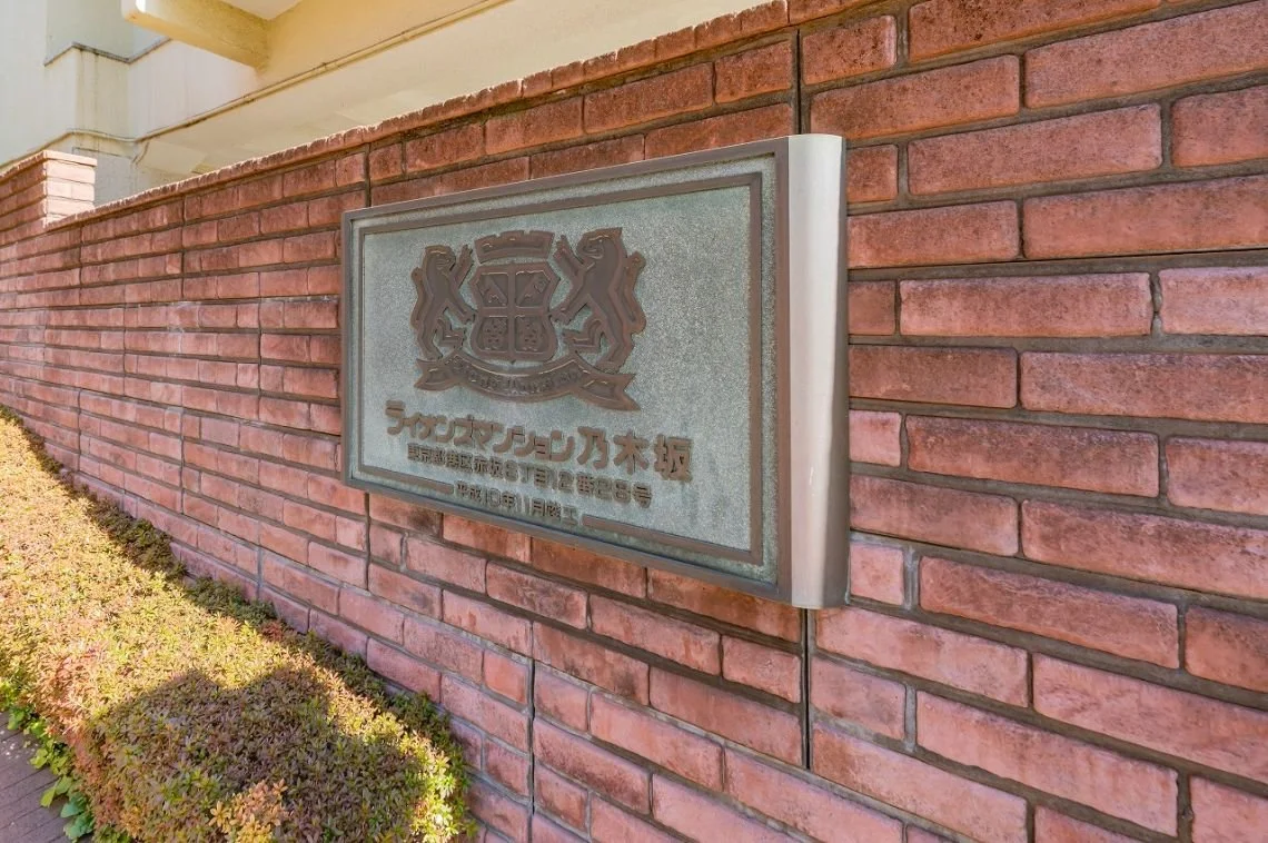 赤レンガの塀に取り付けられた金属製の看板。看板にはロゴと日本語の文字が刻まれている。