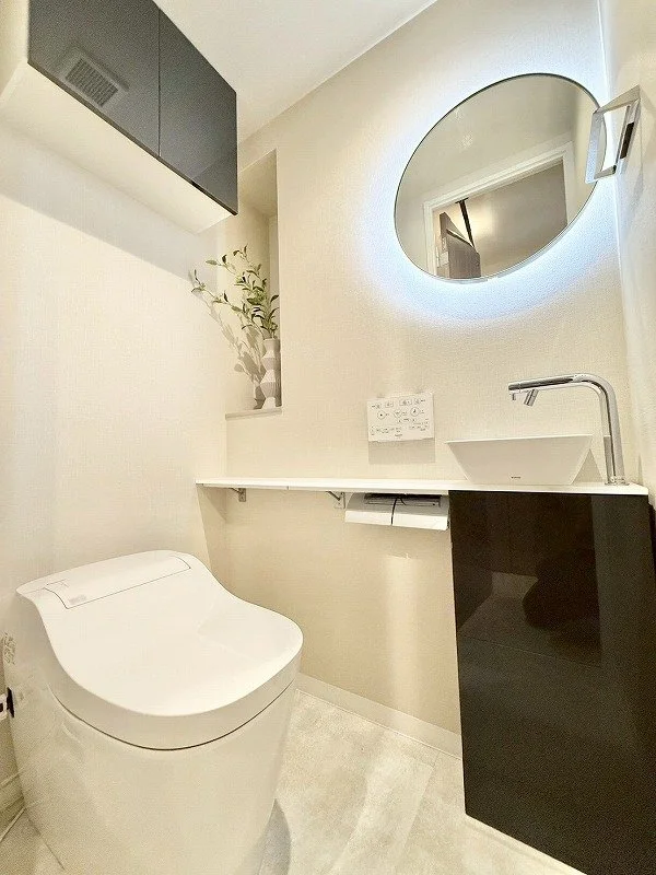 白い便器と白い洗面台、丸い鏡が壁に掛かっているモダンな浴室の interior.