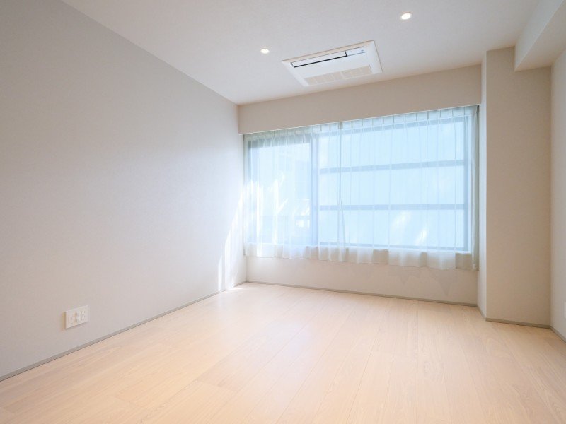 明るい部屋、白い壁と木製の床、大きな窓に薄いカーテン、天井にエアコン。