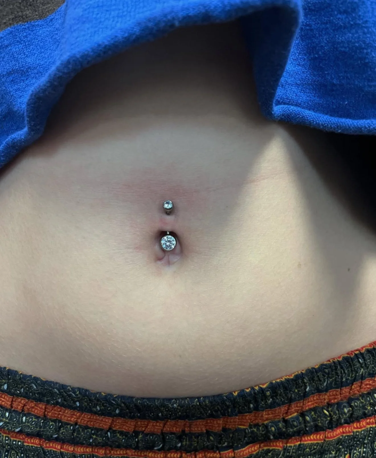 Close-up of a person's belly button with a piercing featuring two diamond-like stones.