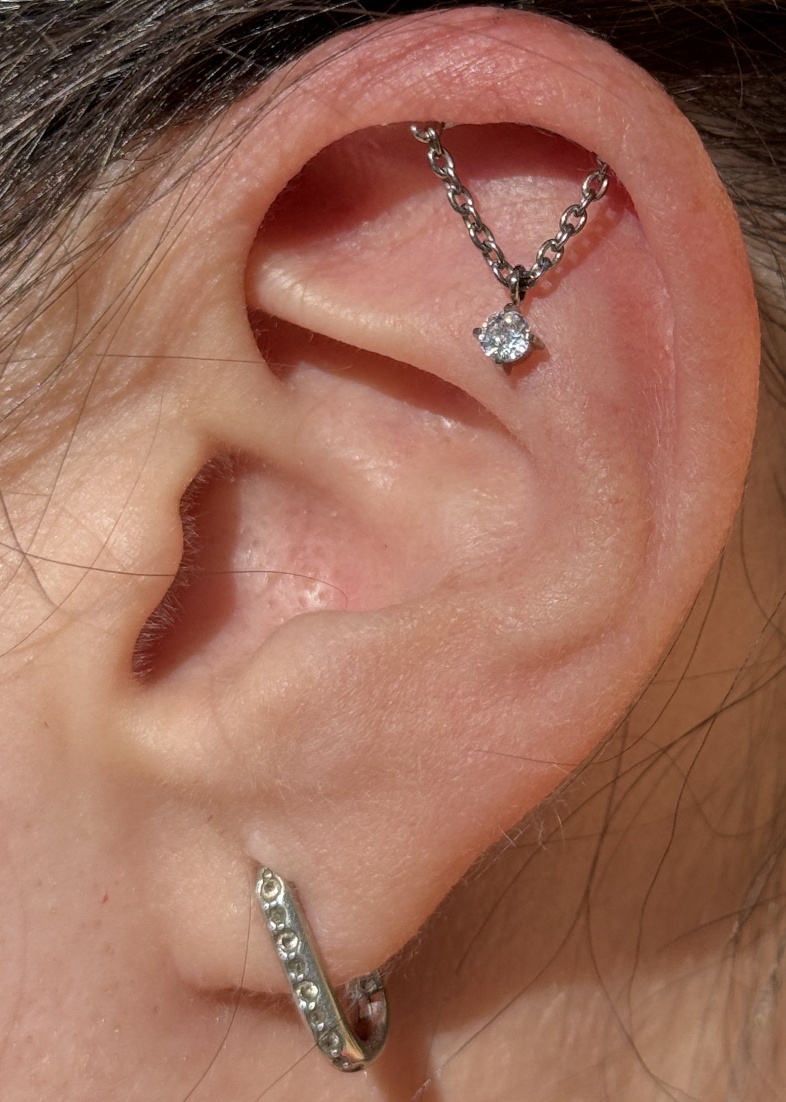 Close-up of a human ear with a dangling diamond earring and a small hoop earring.