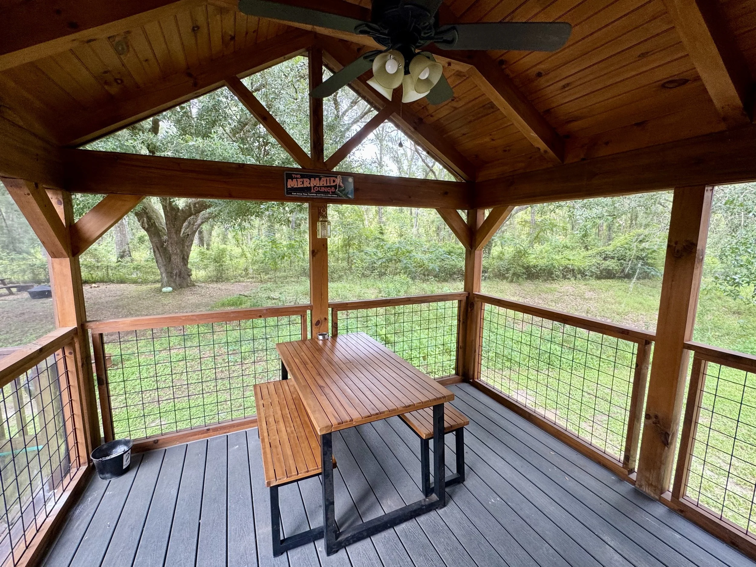 Our screened in outdoor porch with a table, matching benchs, and a decorative decor, lanterns and surrounded by trees.