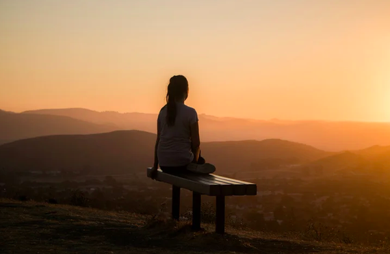 A person sitting on a bench overlooking a sunset over rolling hills and a landscape.