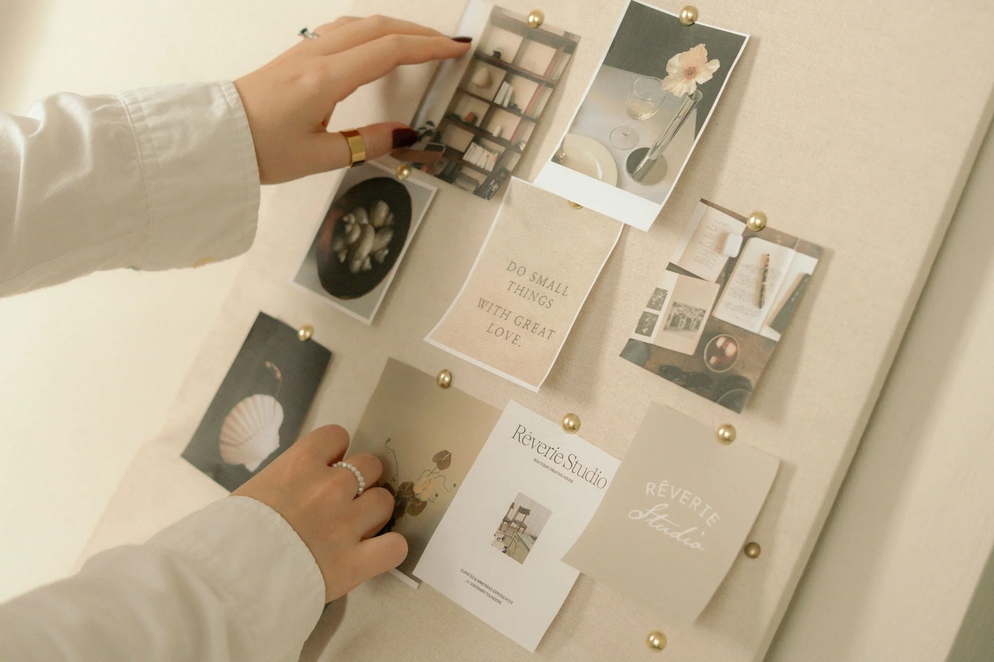 Person pointing at a cork bulletin board with various photographs and paper notes, including one with an inspirational quote.
