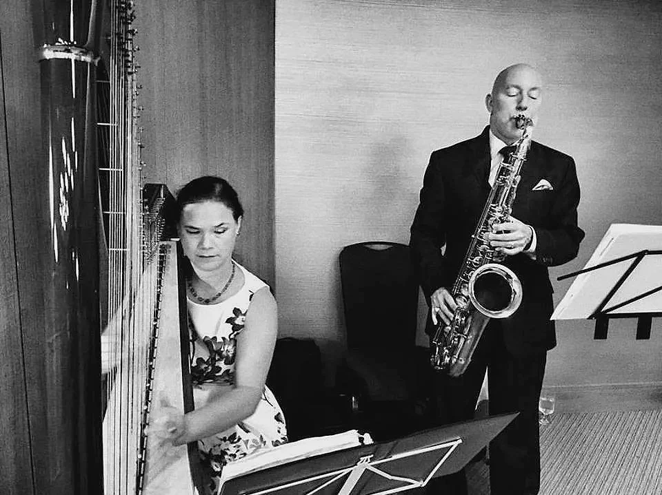 A woman playing the harp and a man playing the saxophone in a room.