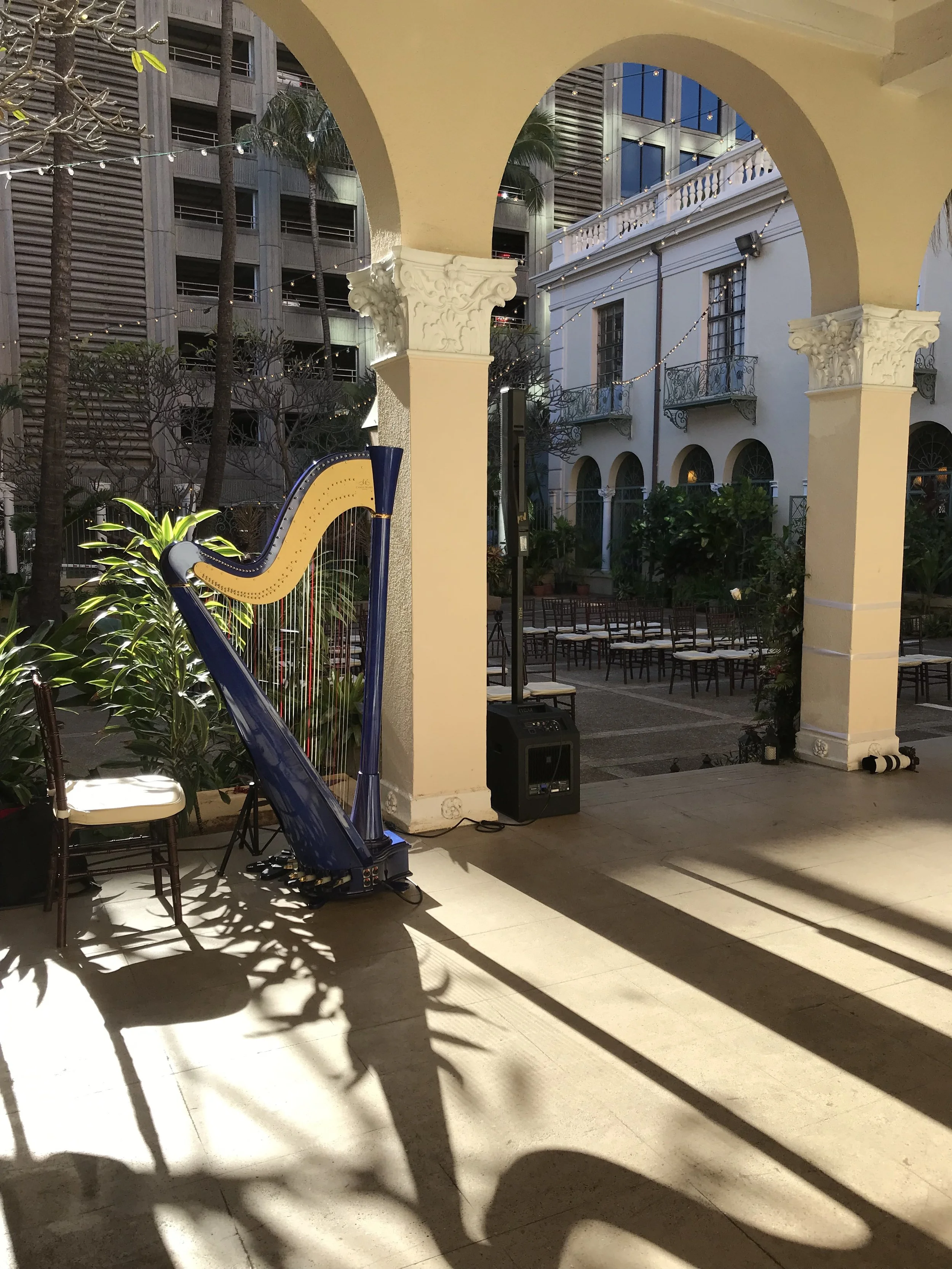 Harp setup with a chair and speaker in an outdoor patio area with arched columns and string lights