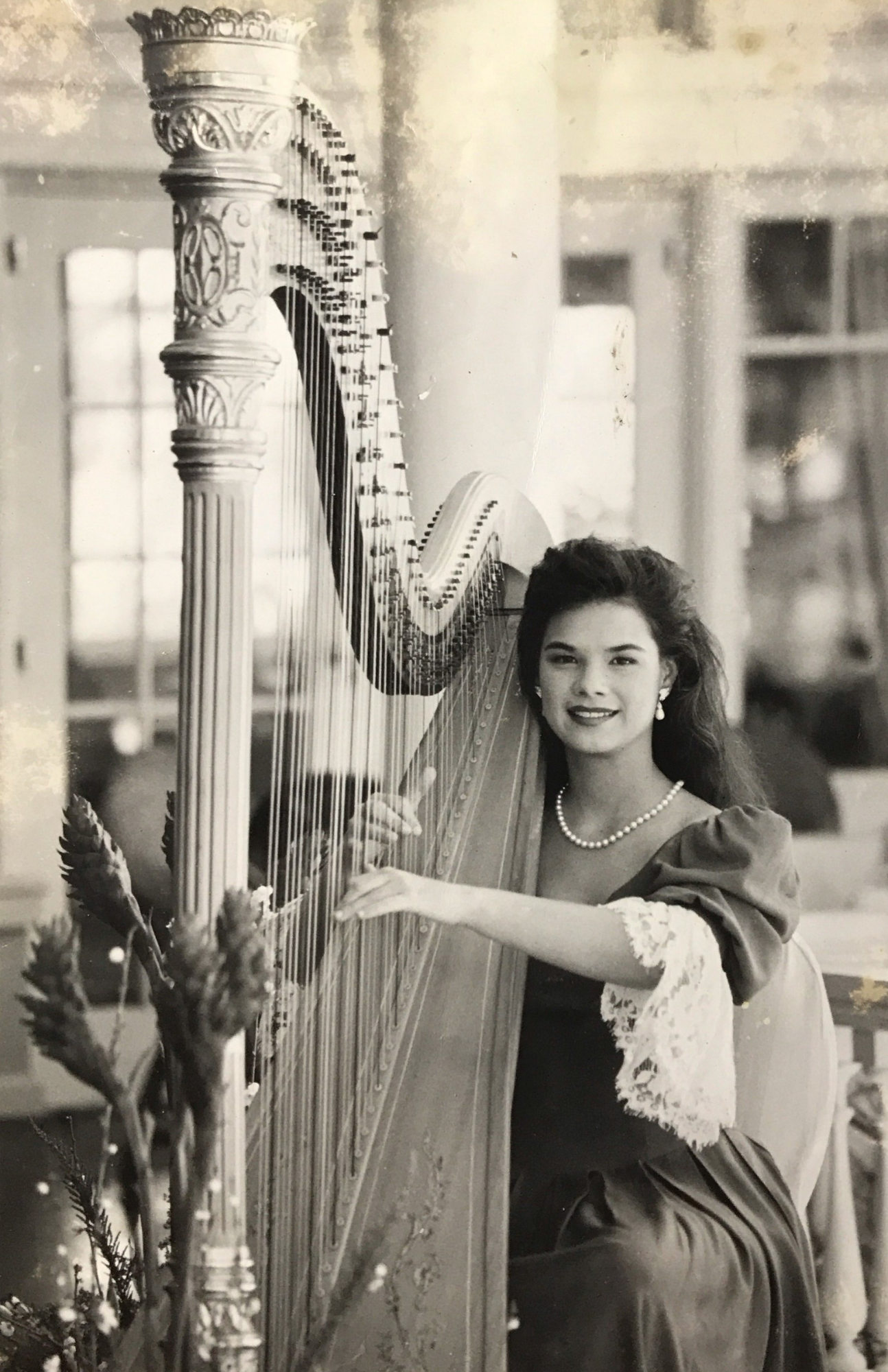 Ready to play her golden harp @ the Moana Hotel's Veranda.  It is a black and white photo with an elegantly dressed Hawaiian harpist.