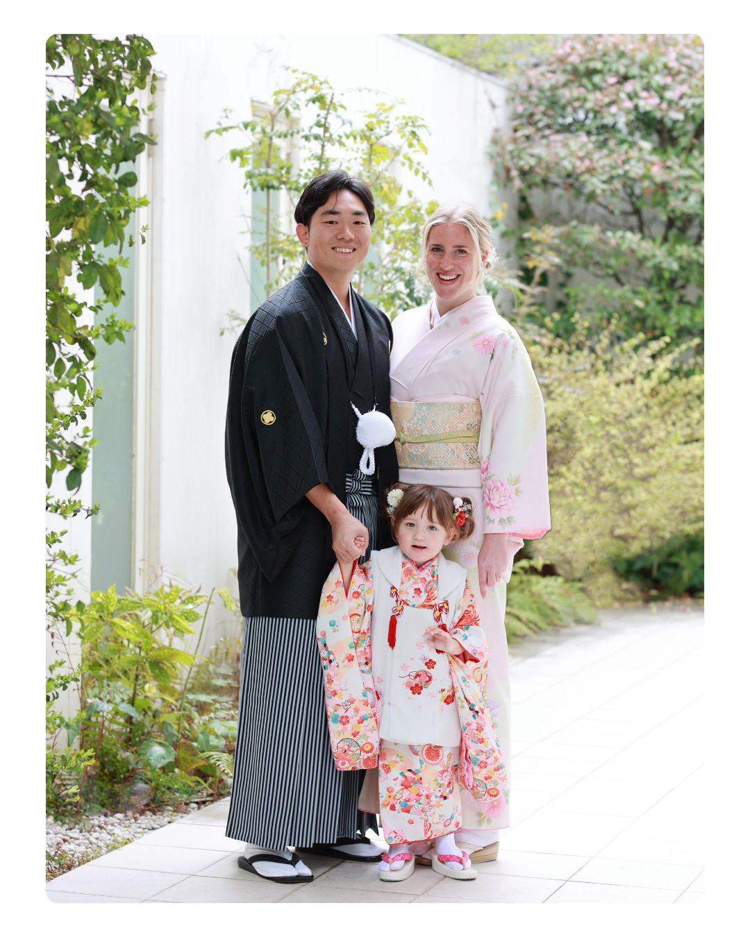 Family dressed in traditional Japanese kimonos standing outdoors in a garden.