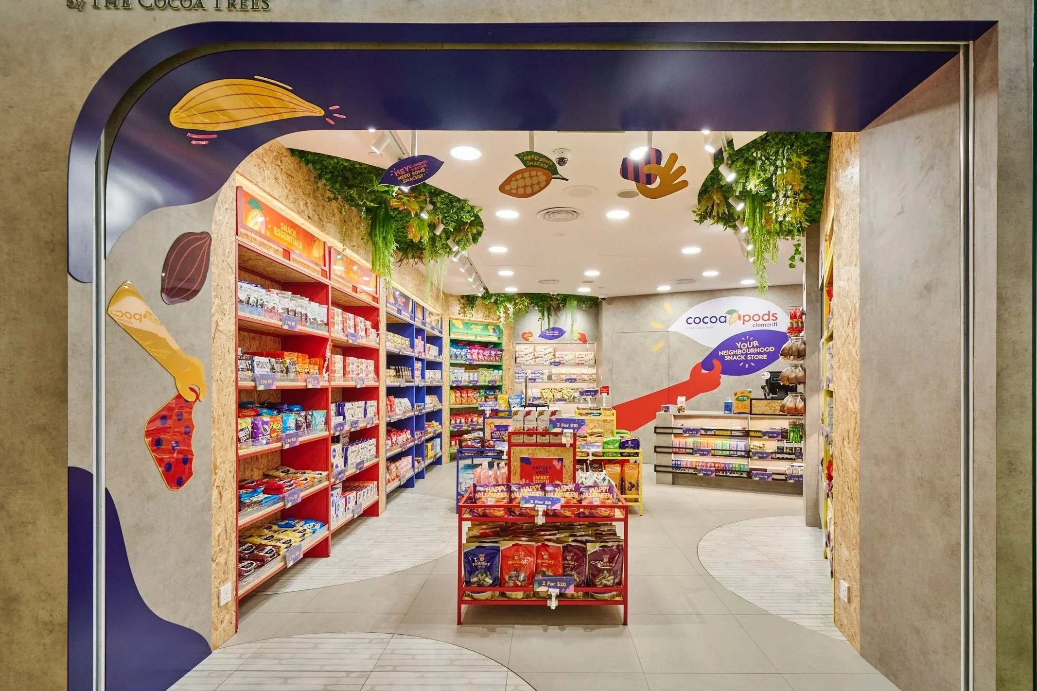 Interior view of Cocoa Pods snack store with shelves of snack products and green decorative plants hanging from the ceiling.
