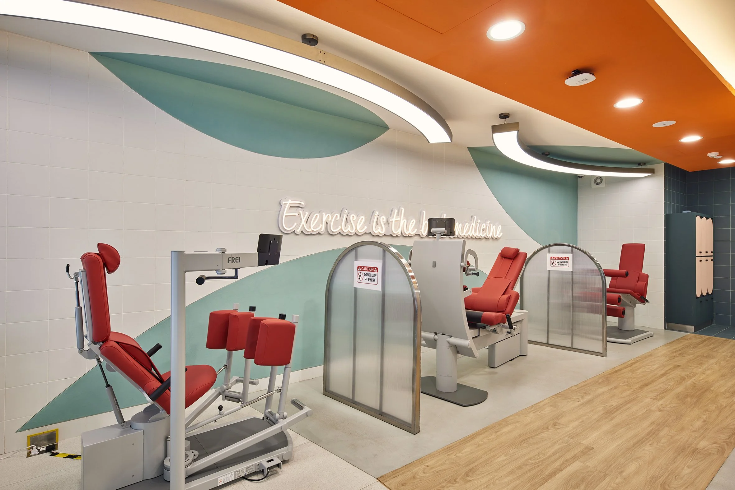 Rehabilitation exercise room with red medical chairs, partitions, and a neon sign that says 'Exercise is the best medicine'.