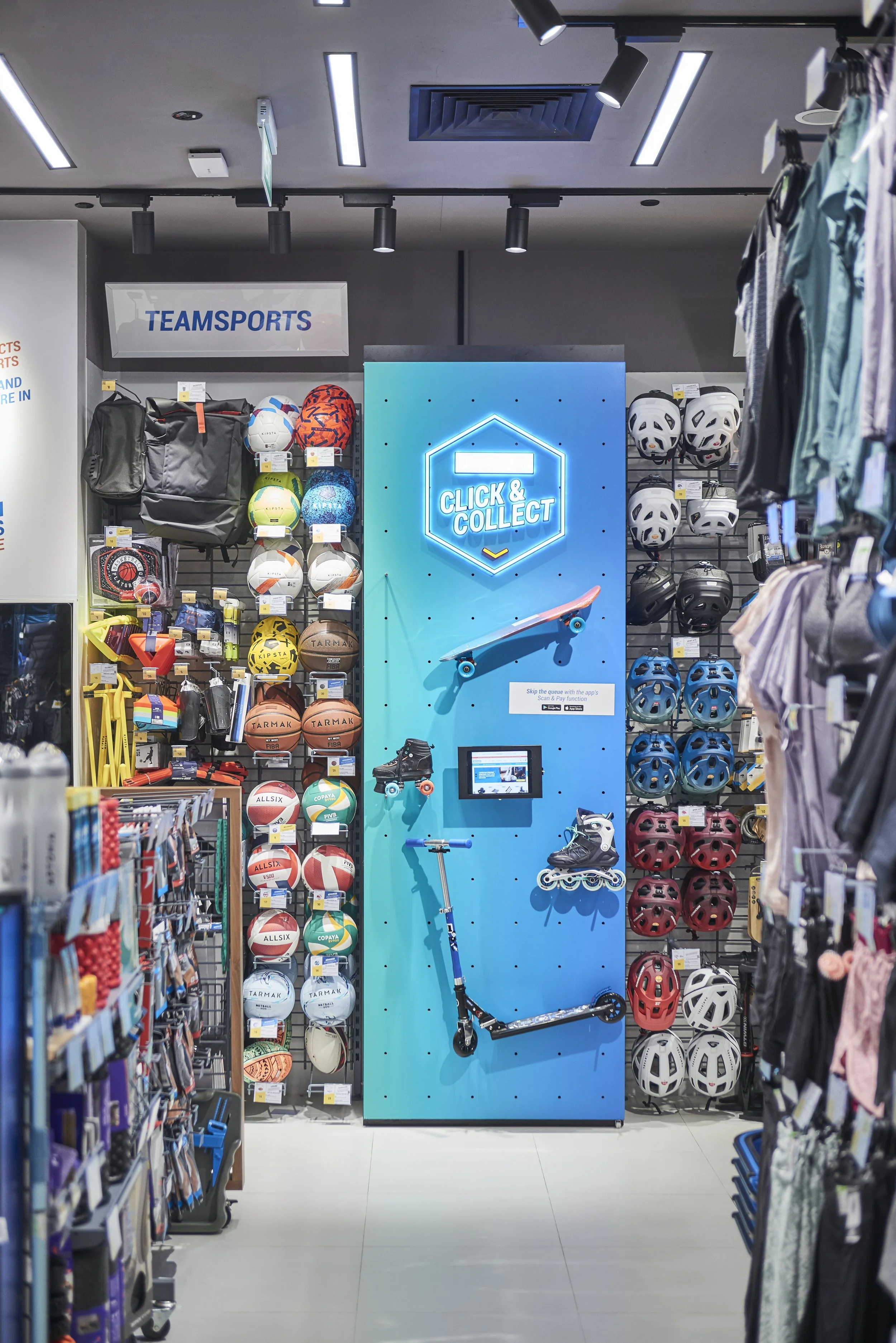 A sports equipment store display features a blue wall with roller skates, a scooter, and a mounted skate lane, with helmets, basketballs, and other sports gear on shelves around.