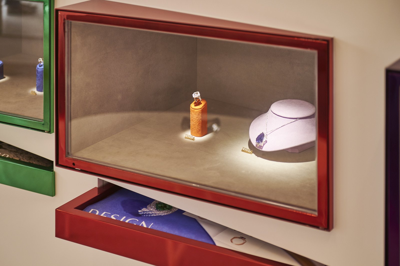 Jewelry display case with a diamond ring on an orange stand and a necklace with purple stone on a white jewelry bust.