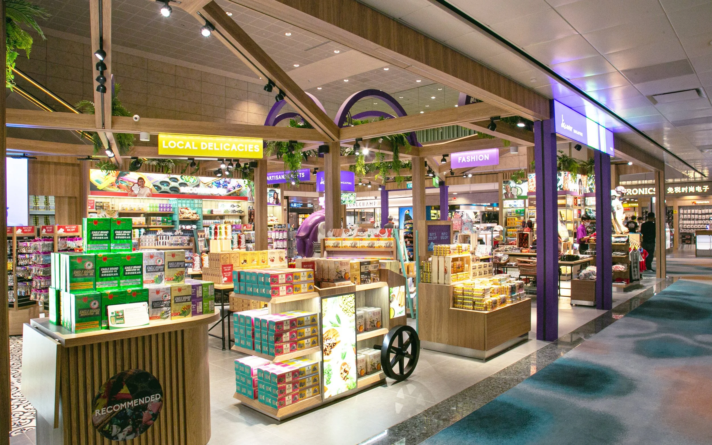 Interior of a shopping mall with a store section labeled 'Local Delicacies,' featuring shelves stocked with various snack boxes, and other stores visible in the background.