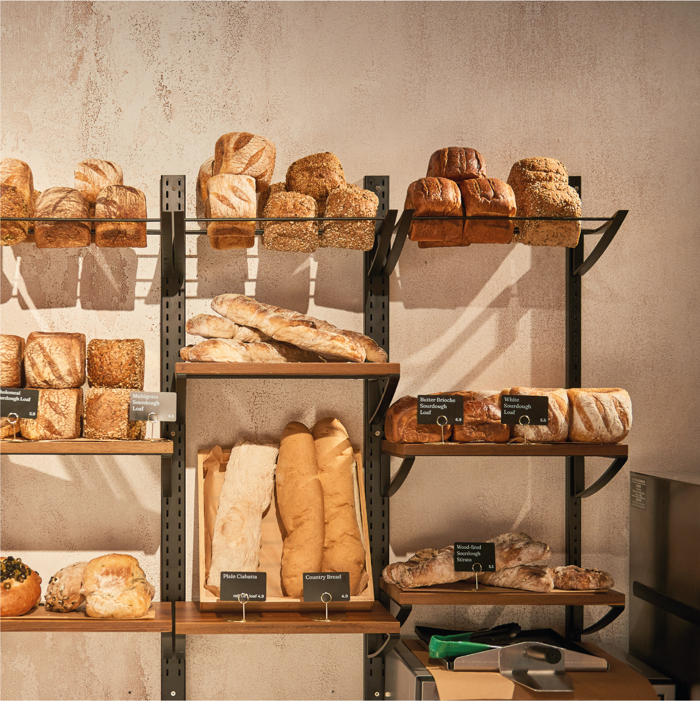 Shelves displaying various types of bread including loaves, baguettes, and rolls in a bakery.