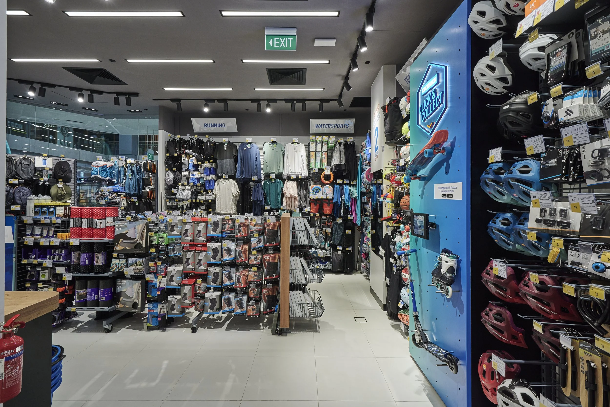A retail store section with outdoor sports gear, including helmets, cycling accessories, and athletic clothing, with signs labeled "Running" and "Watersports."