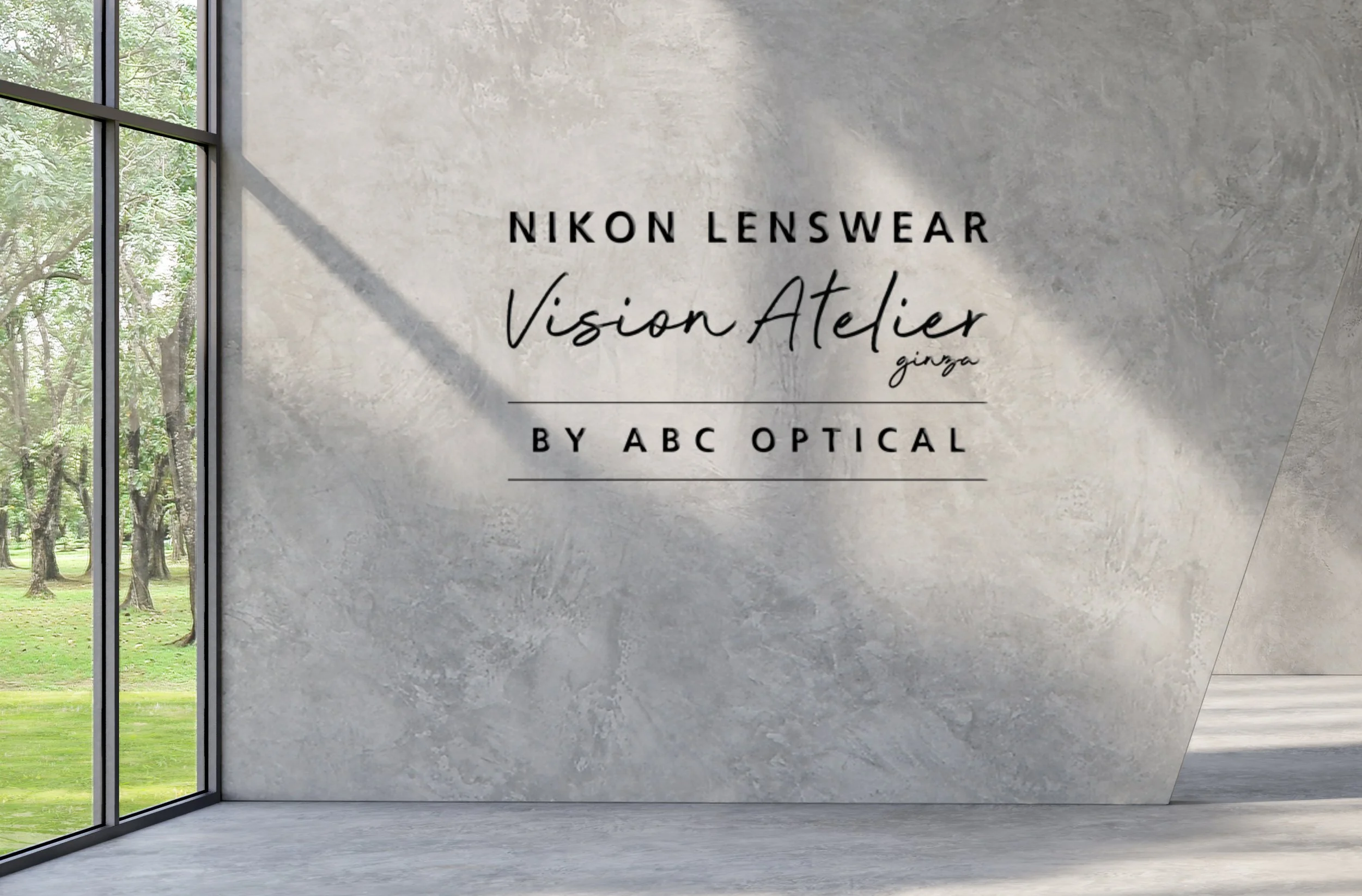 Sign on a concrete wall reading 'Nikon Lenswear Vision Atelier by ABC Optical' with large windows showing a park outside.