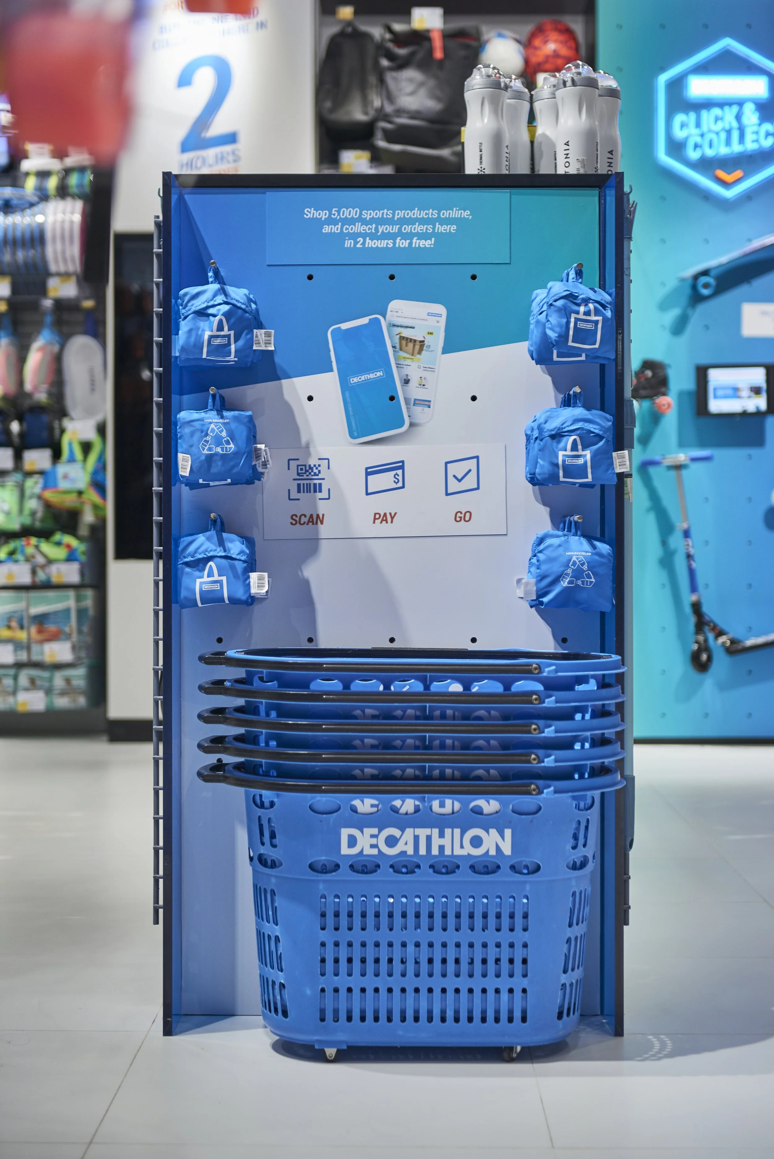 Decathlon's self-scanning shopping station with blue bags, hand baskets, and digital instructions for shopping, payment, and checkout.