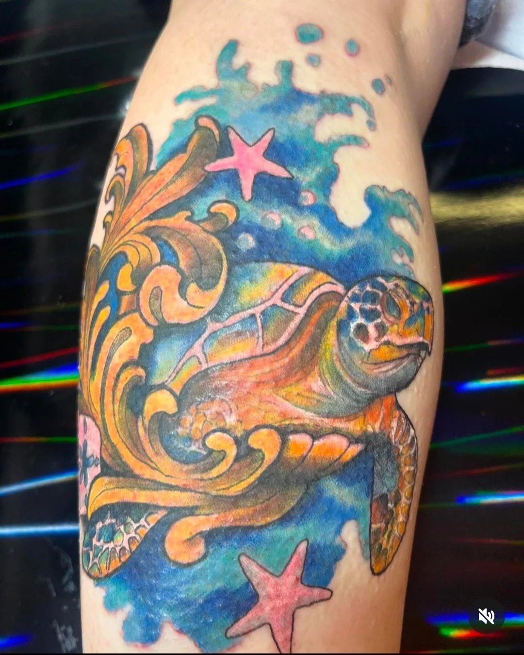 Colorful tattoo of a sea turtle surrounded by ocean waves, starfish, and a blue background.