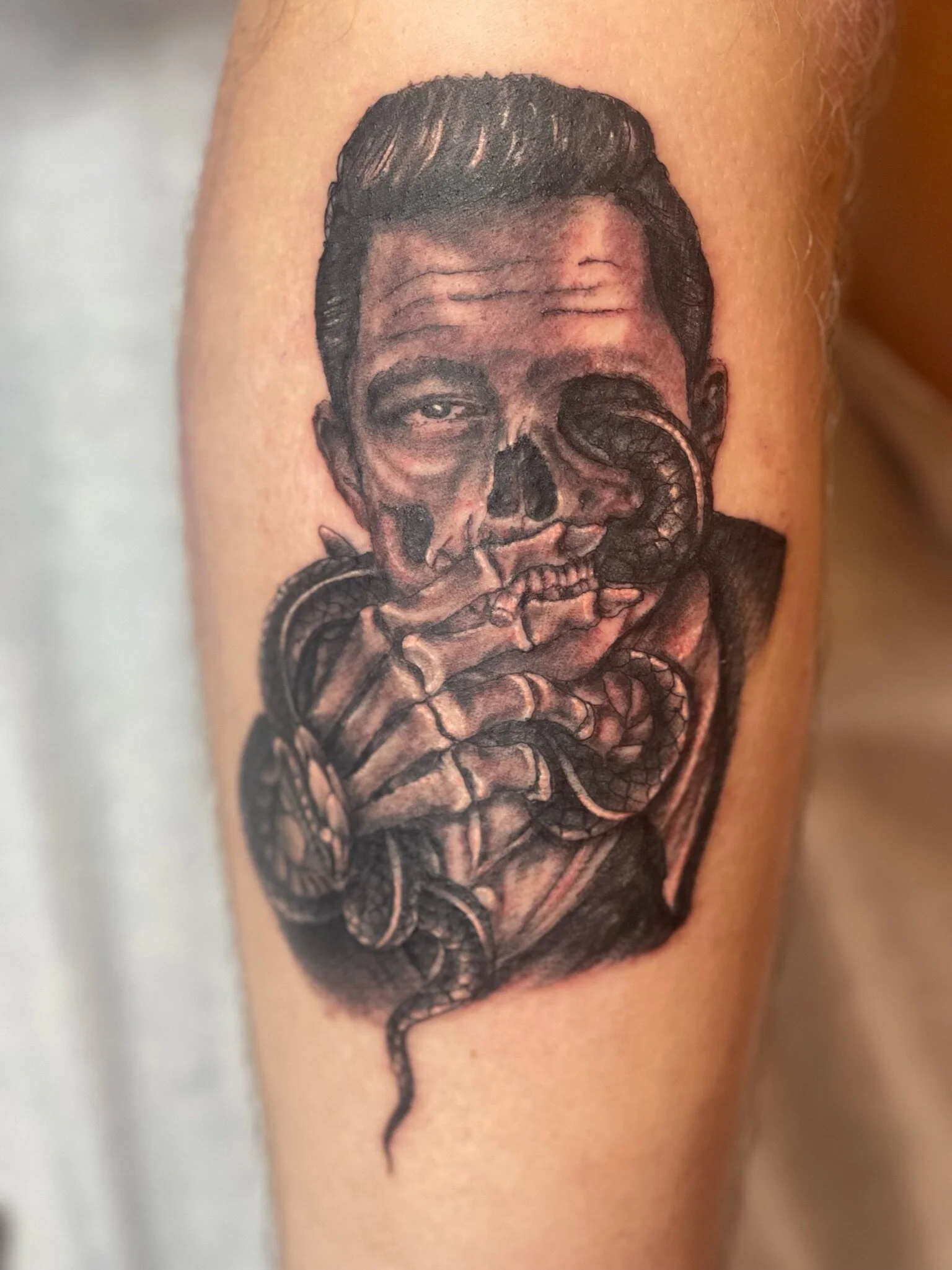 Tattoo of a man's face with part of his skull exposed, intertwined with a coiled snake.