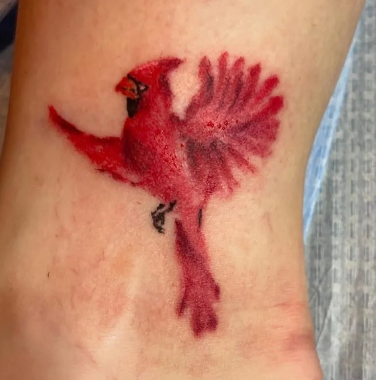 A tattoo of a red and black bird, with detailed feathers, on someone's skin.