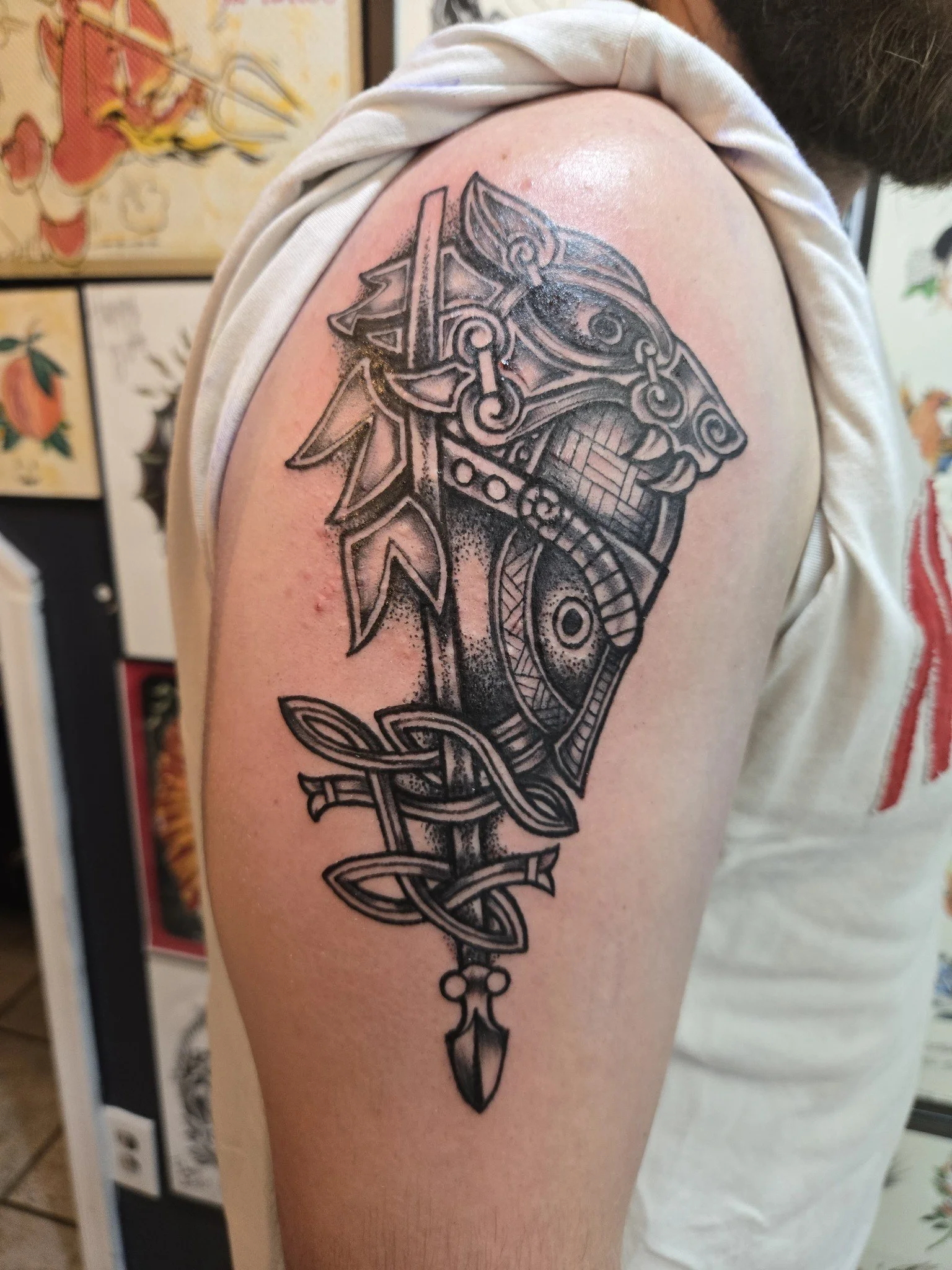 Black ink tattoo of a Viking helmet with intricate knotwork and a sword on the arm.