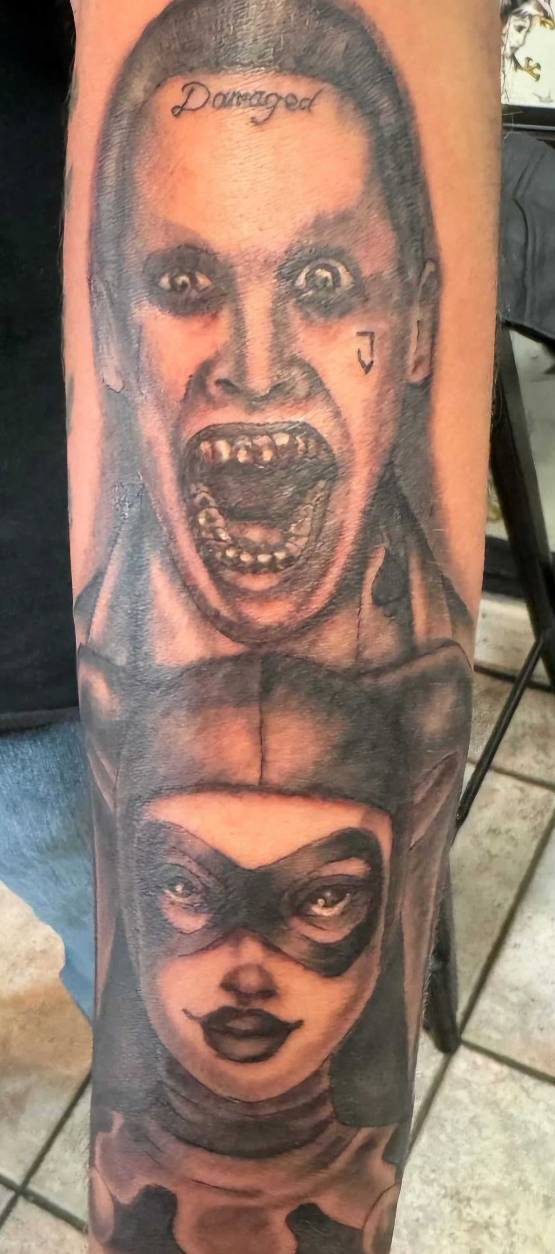Tattoo depicting two faces, the top is a screaming man with a damaged smile and the word 'Danger' on his forehead, the bottom is a woman with a mask and dark lipstick.