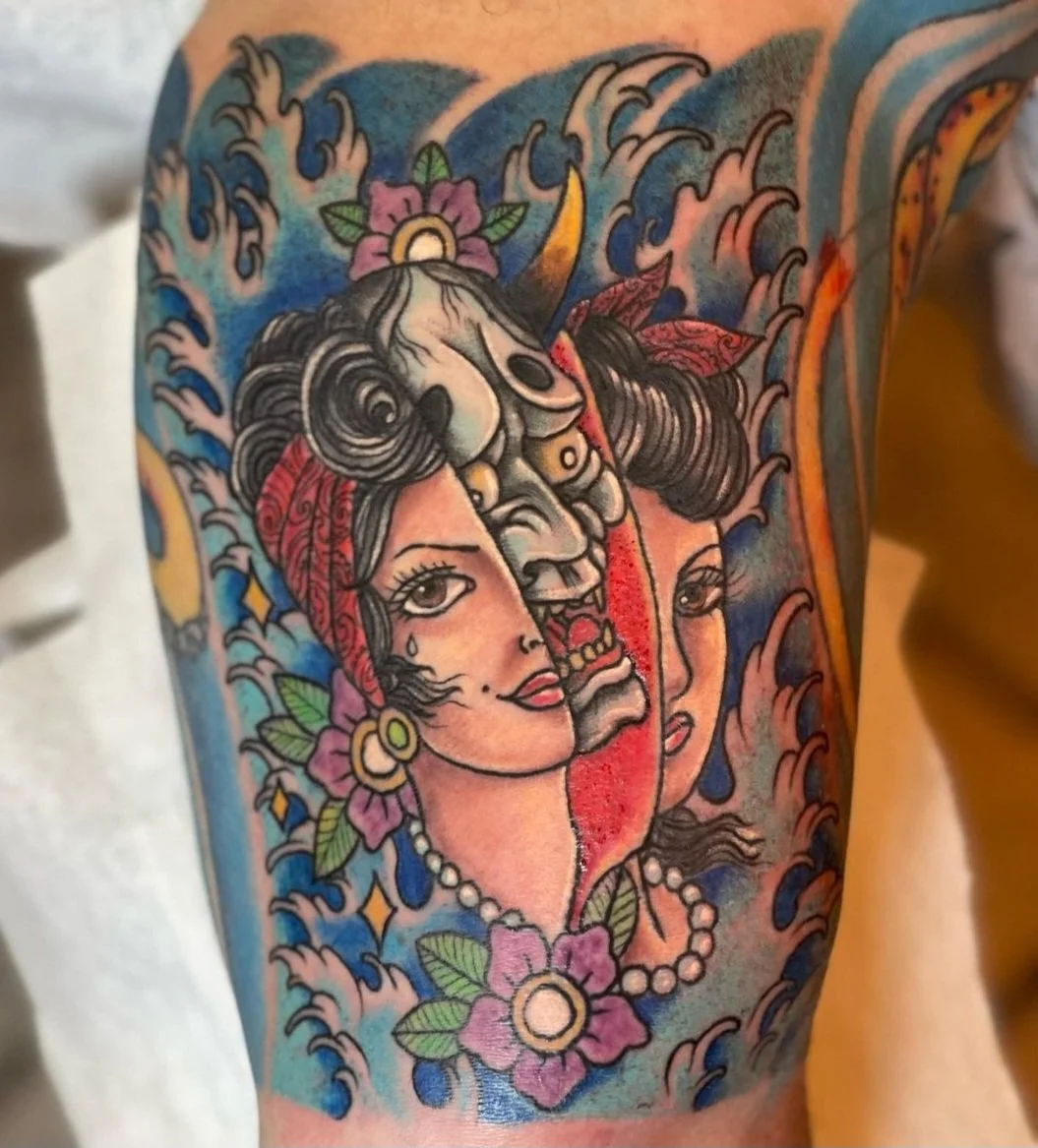 Colorful tattoo featuring a woman's face with flowers, a skull, and ocean waves in a traditional tattoo style.