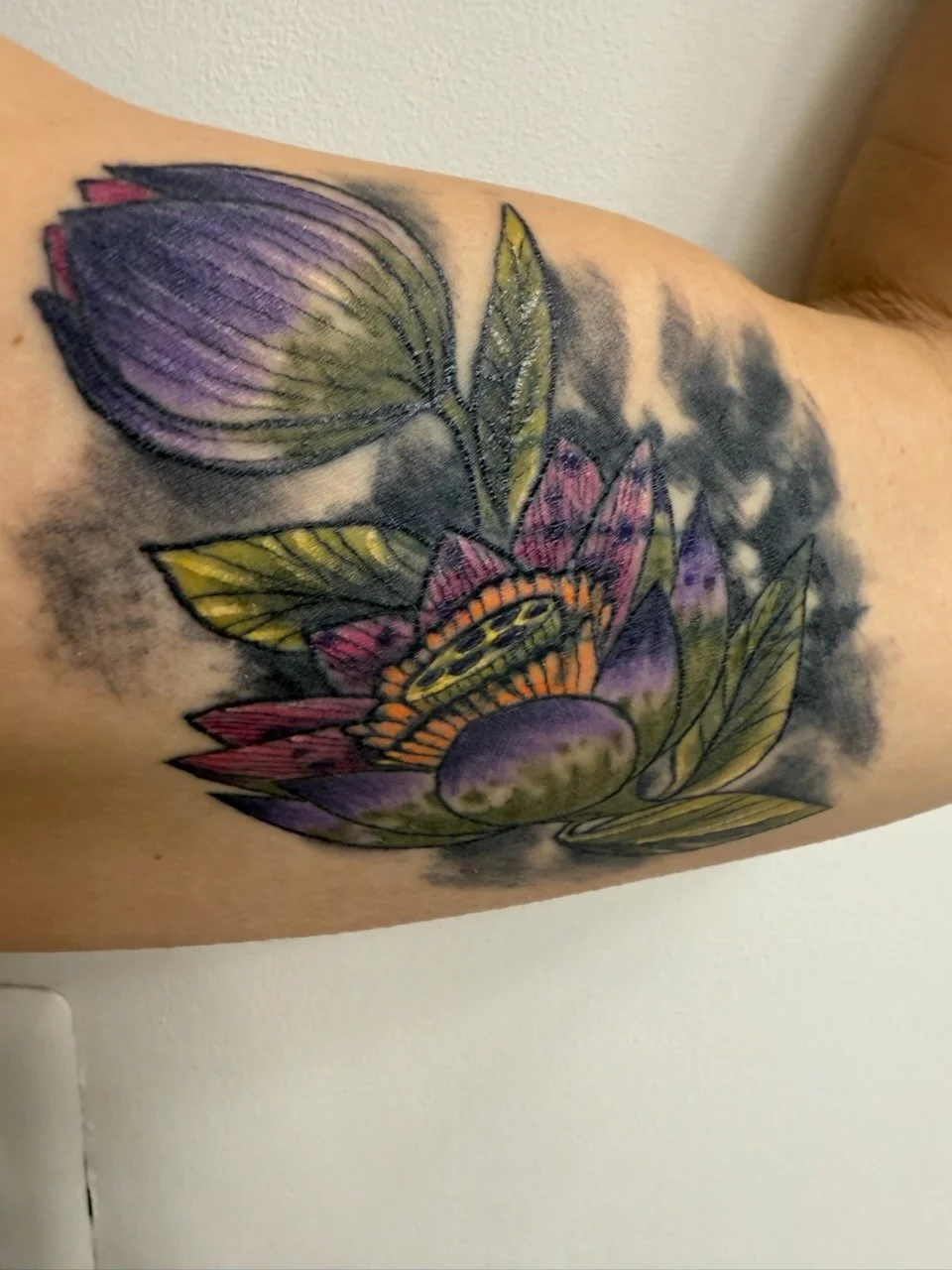 Colorful tattoo of flowers and leaves on person's upper arm.