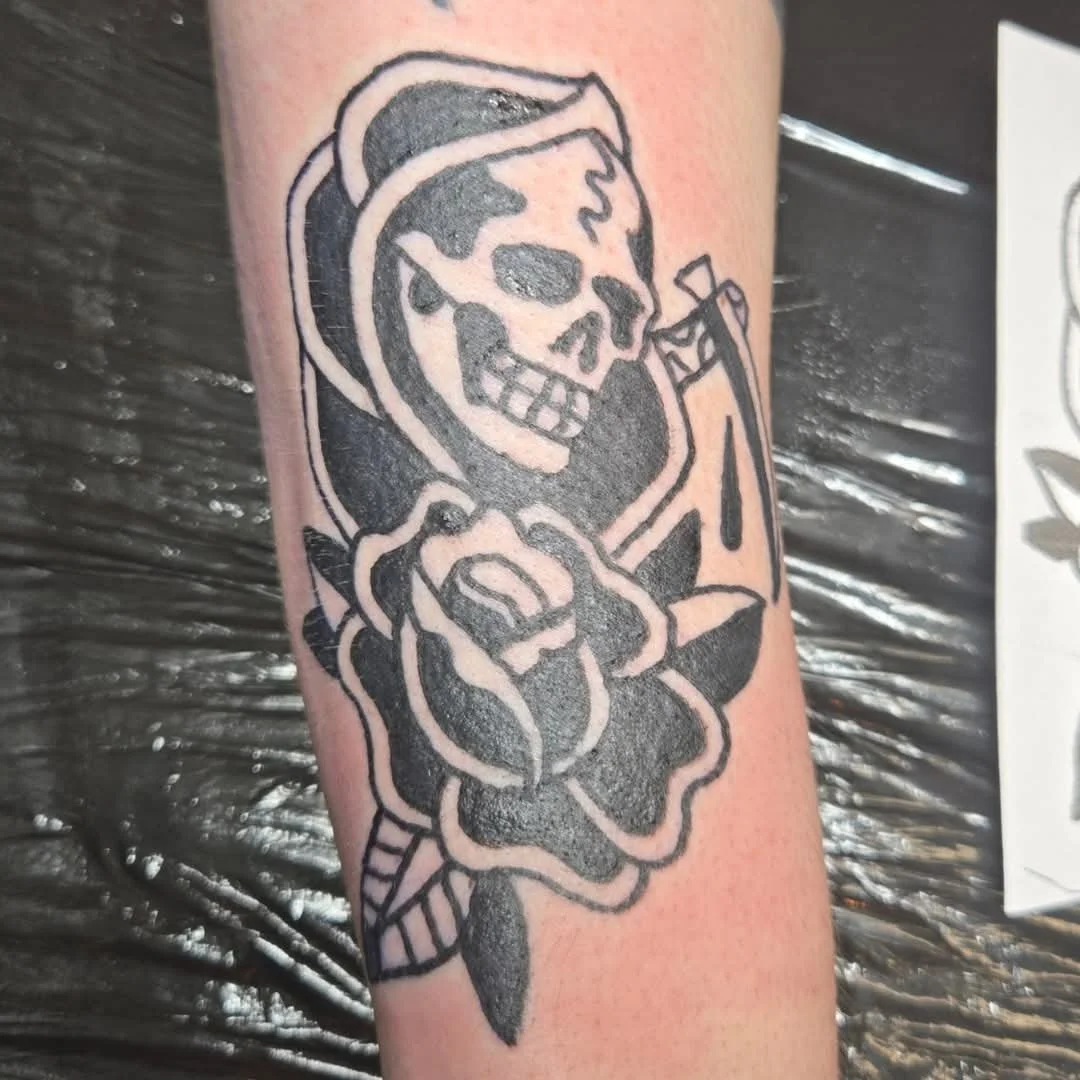 Black outline tattoo of a skeleton with a flower and a cigarette.