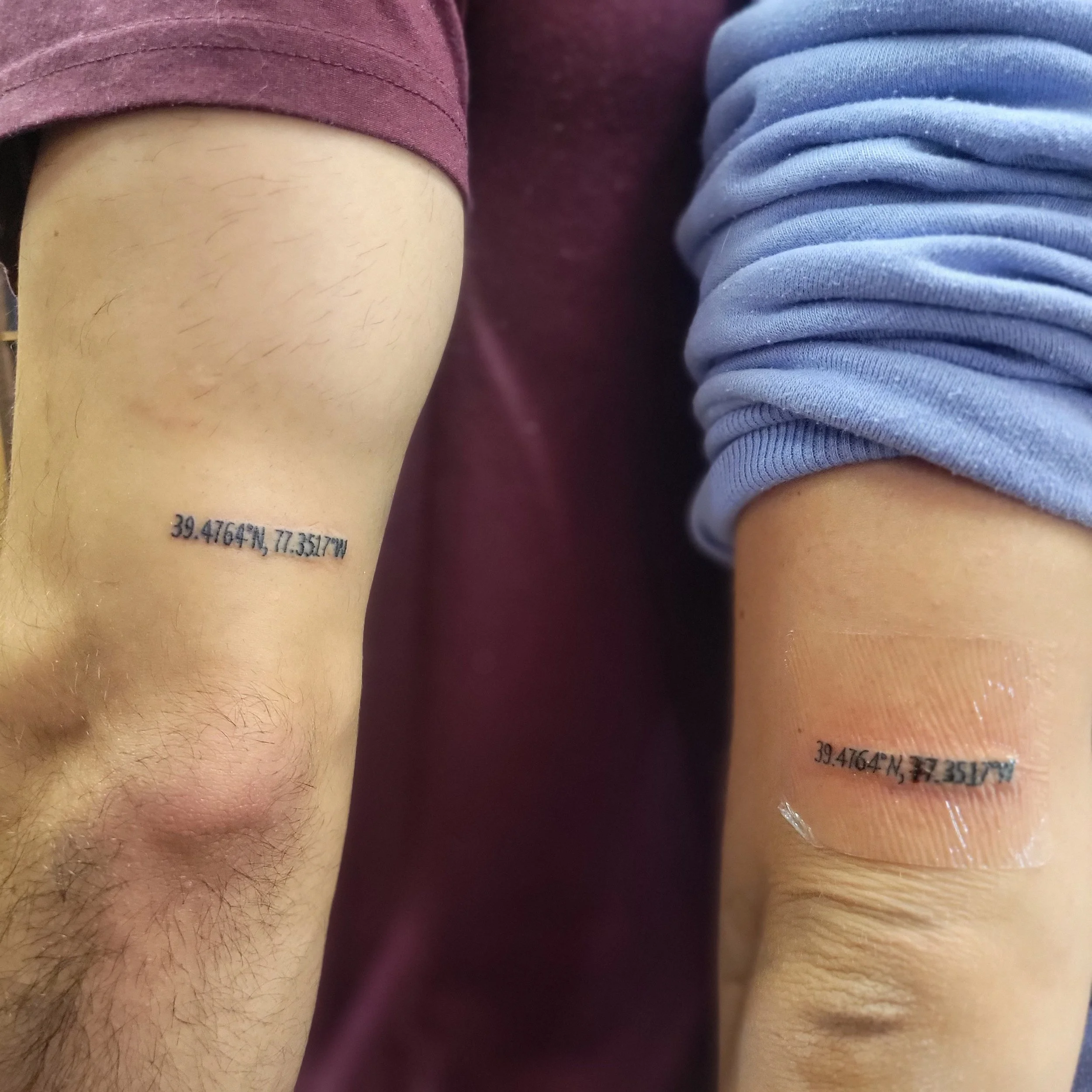 Two forearms with tattoos of the same coordinates, one with hair and the other with a bandage around the wrist.