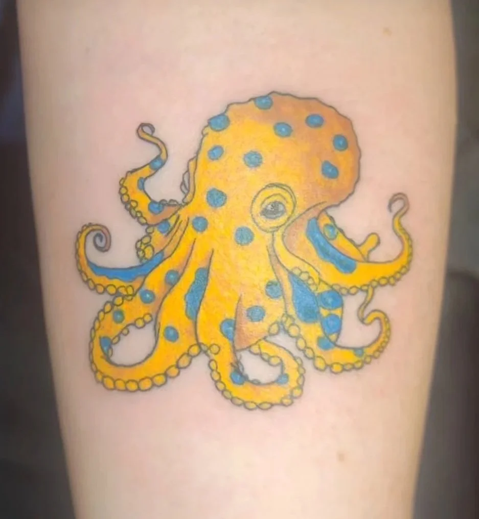 Colorful tattoo of a yellow octopus with blue spots on skin.