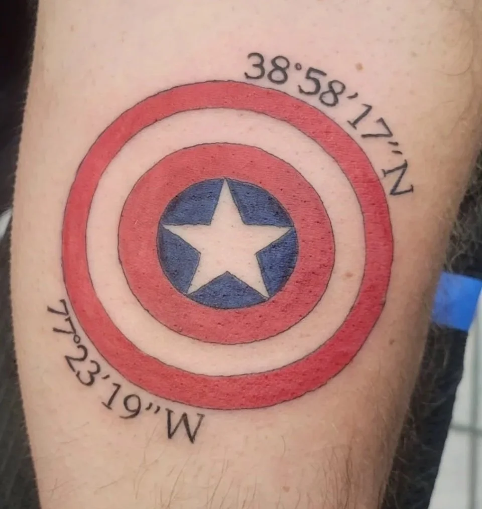 Tattoo of Captain America's shield on arm, with coordinates 38°58'17"N, 77°23'19"W.