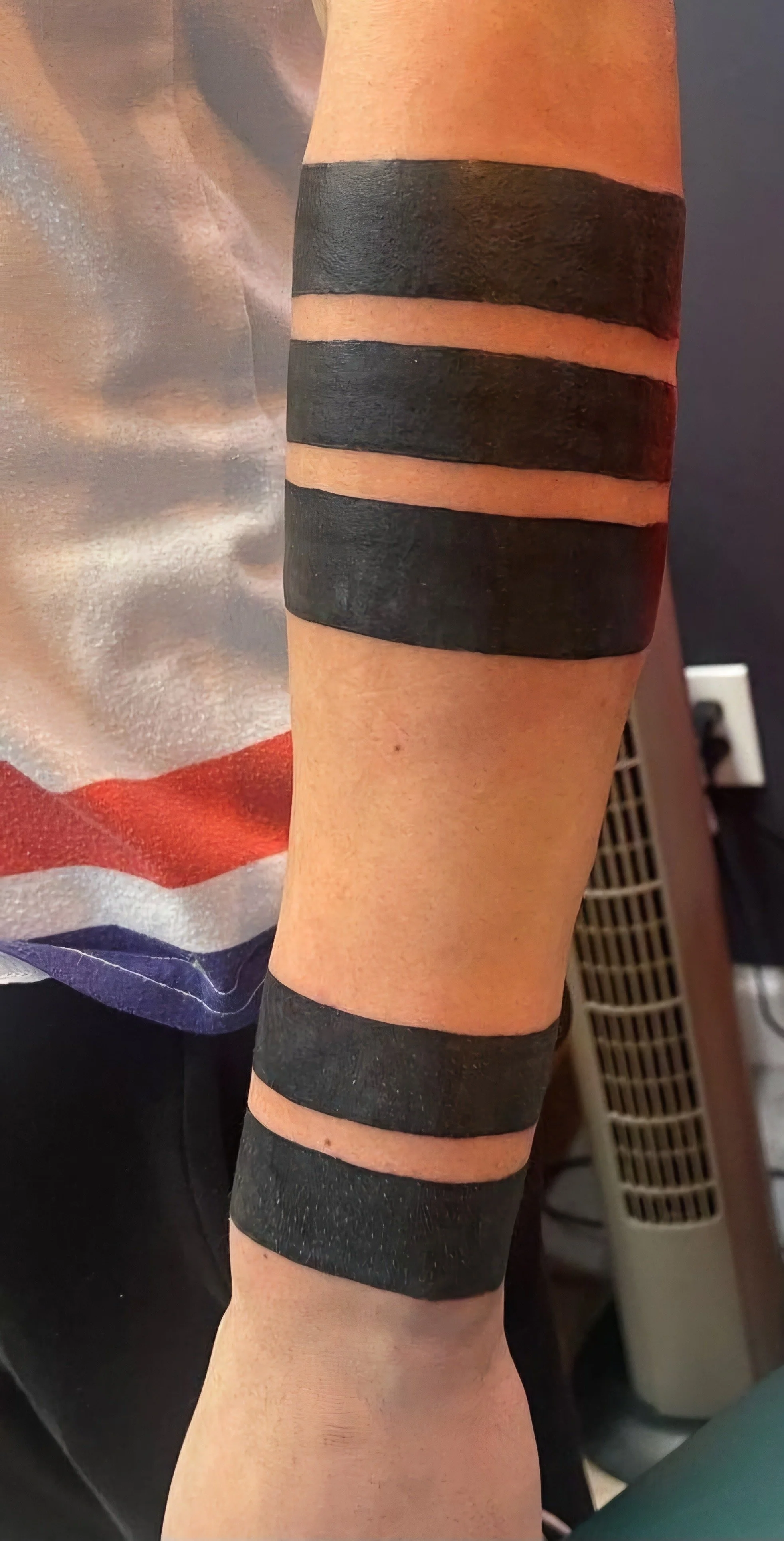 Close-up of a person's forearm with black tape wrapped around the upper and lower parts of the arm, above and below the elbow.