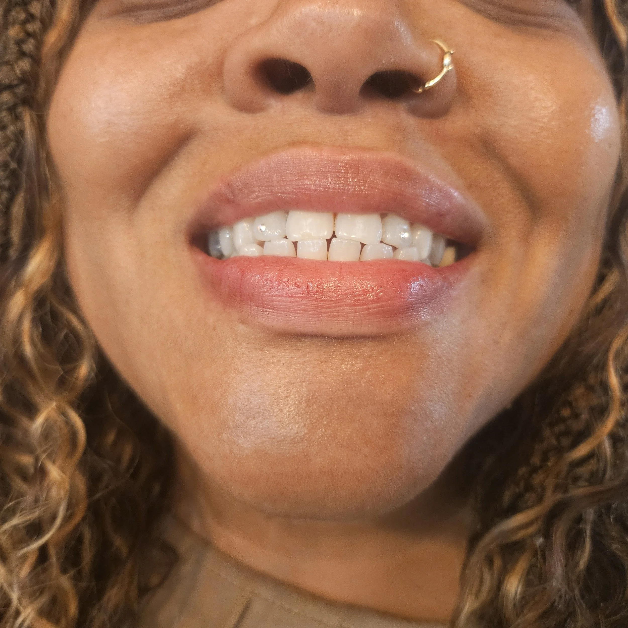 Close-up of a woman smiling, showing her teeth, with a nose ring and curly hair.