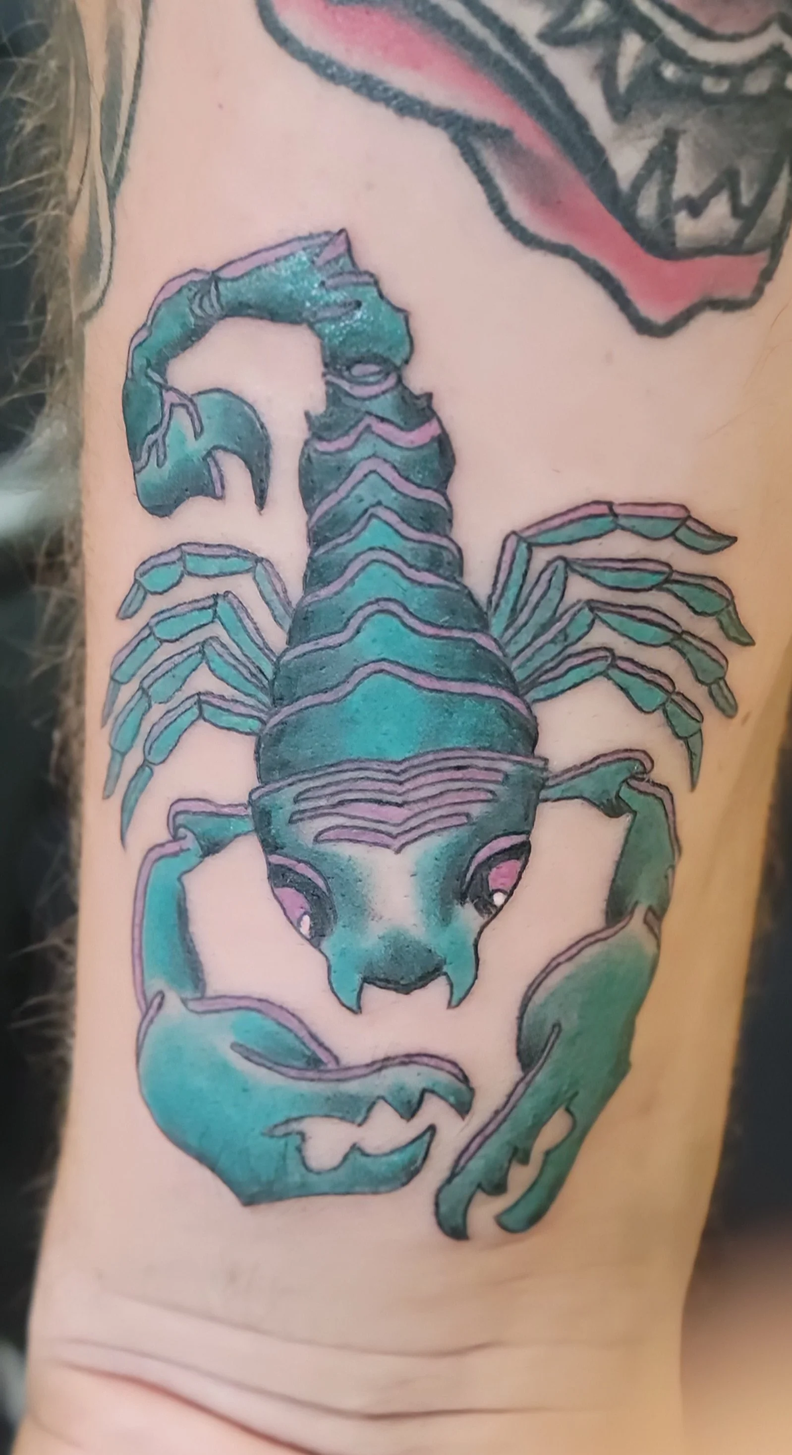 Tattoo of a blue-green scorpion with a dog's face on its tail, on person's arm.