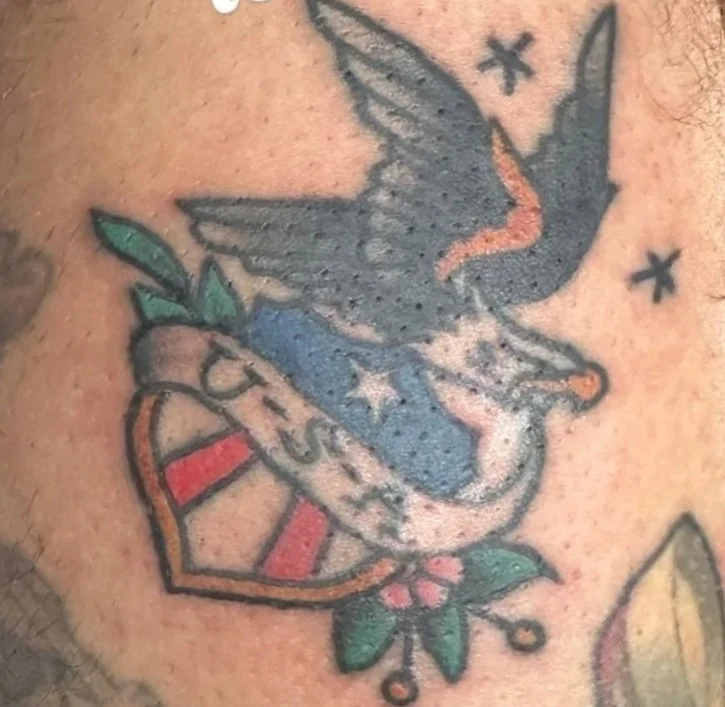 Tattoo of a swallow with an American flag, a red and white striped shield, and flowers.
