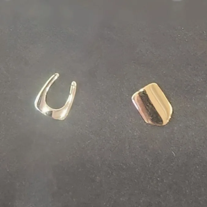 A silver U-shaped object and a sliced cake with layers of yellow, pink, and dark brown on a dark surface.