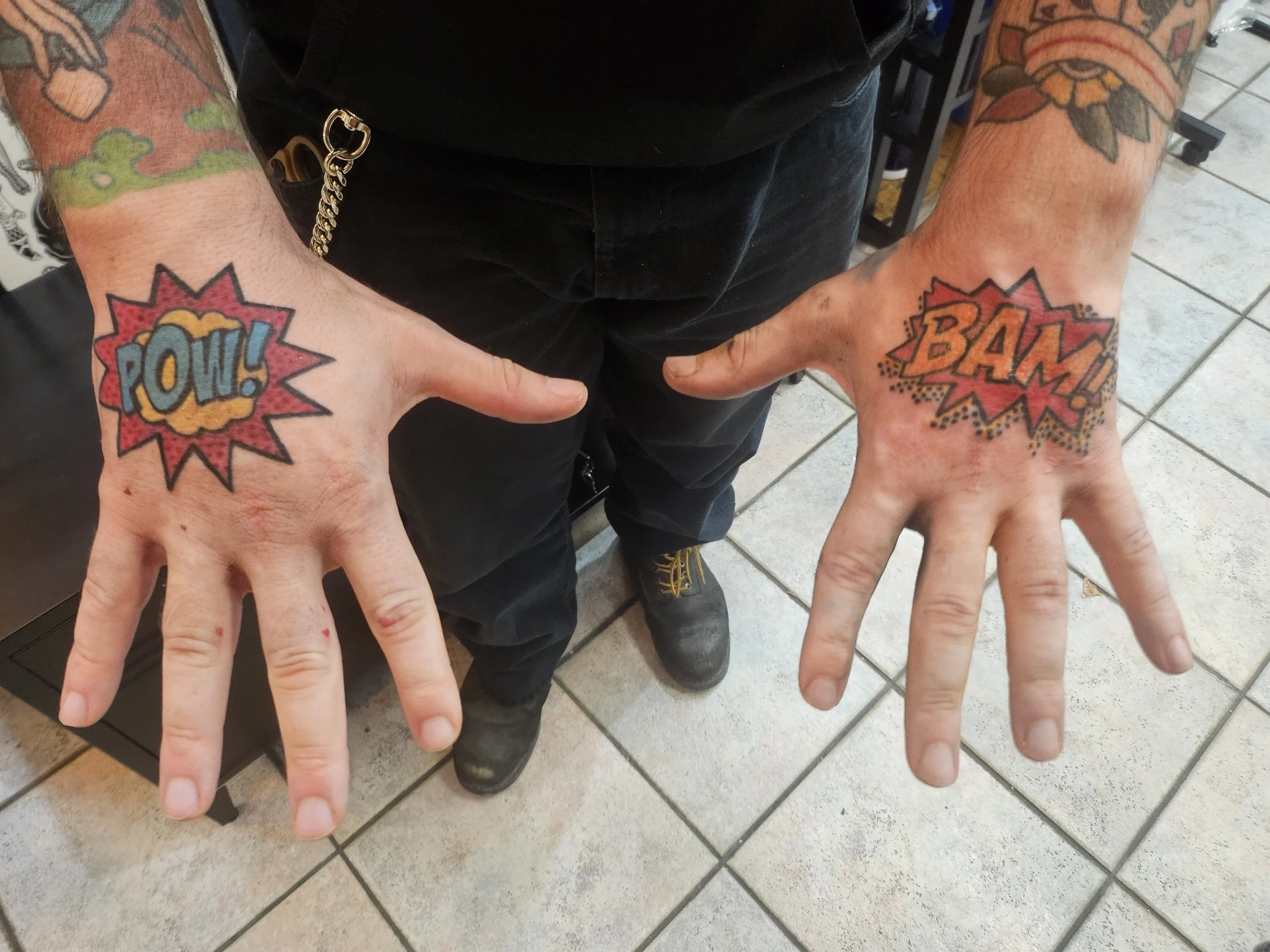 Person showing tattoos of comic book style words on their hands: 'POW!' on the left hand and 'BAM!' on the right hand.