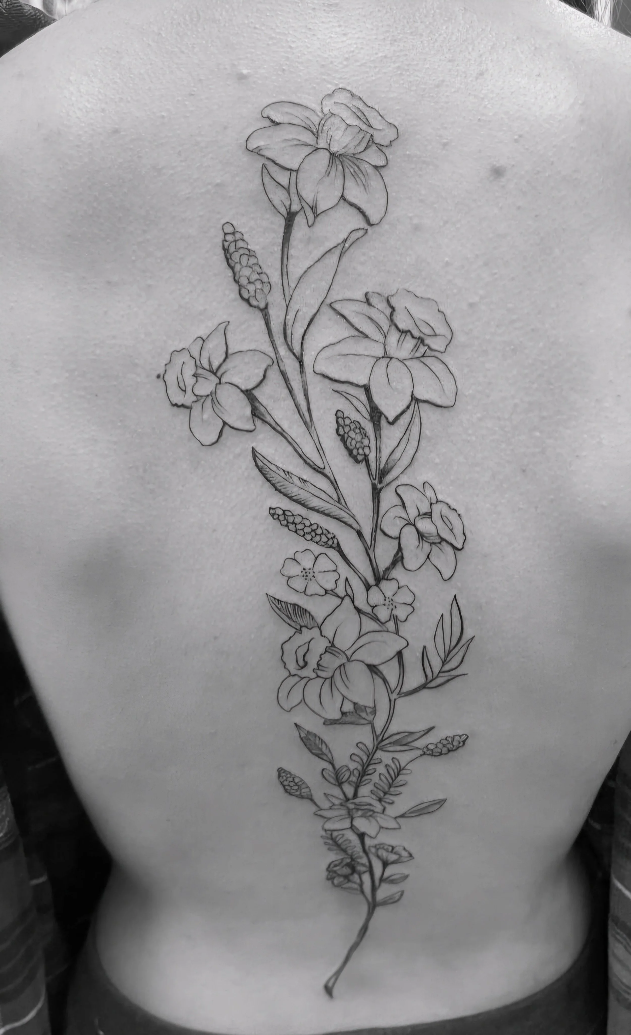 Tattoo of a vertical floral design with various flowers and leaves on a person's back.